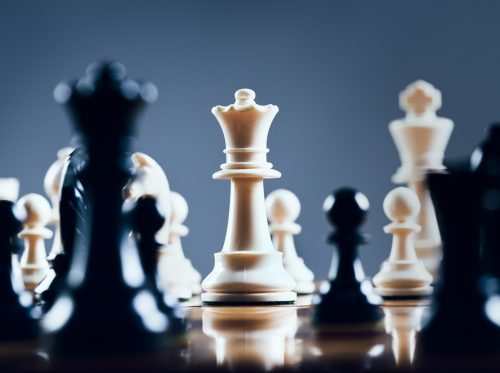 Close up of chessmen on chessboard, with the focus on the centrally placed white queen.